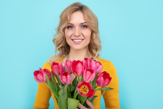 Glückliche junge Frau mit Frühlingstulpenblumen auf blauem Hintergrund 8. März