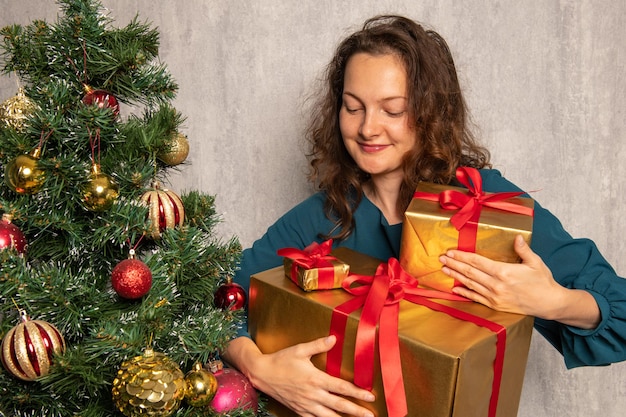 Glückliche junge Frau mit Geschenken des neuen Jahres nahe Weihnachtsbaum