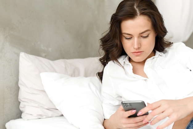 Glückliche junge Frau mit Handy auf dem Sofa liegend Junge glückliche Frau legt sich aufs Bett und durchsucht soziale Netzwerke zu Hause auf dem Smartphone