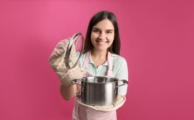 Glückliche junge Frau mit Kochtopf auf rosa Hintergrund