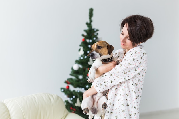 Glückliche junge Frau mit reizendem Hund im Wohnzimmer mit Weihnachtsbaum. Urlaubskonzept.