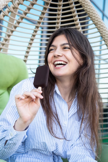 Glückliche junge Frau mit Schokoladeneis in einer Hängematte
