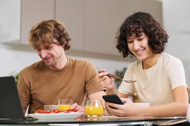 Glückliche junge Frau mit Smartphone, die Cornflakes mit Milch isst