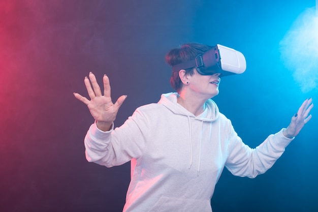 Glückliche junge Frau mittleren Alters, die ein Virtual-Reality-Headset auf rot-blauem Hintergrund verwendet