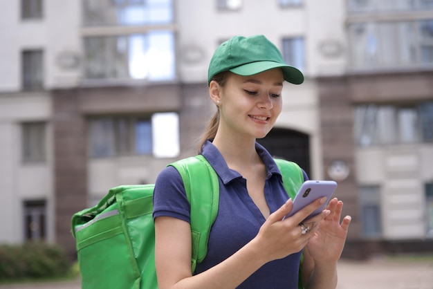 Foto glückliche junge frau oder teenagerin kurier in grüner uniform mit großer thermo-tasche oder rucksack liefern