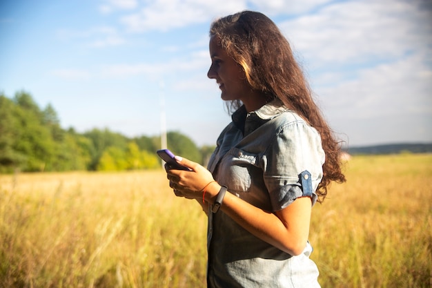 glückliche junge Frau schaut an einem sonnigen Tag in Smartphone auf Naturhintergrund