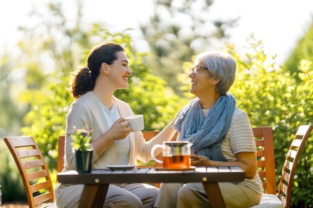 Glückliche junge Frau und ihre Mutter trinken Tee am Sommermorgen Familie sitzt im Garten