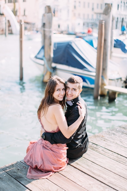 Glückliche junge Frau und Mann, die umarmen und küssen, sitzen auf der Brücke in Venedig, Italien