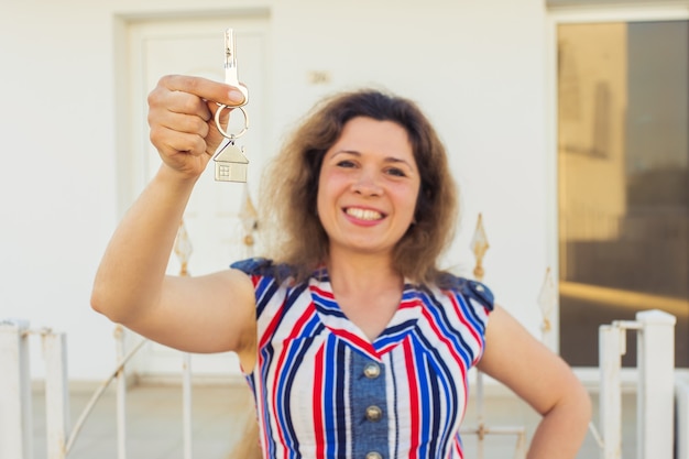Glückliche junge Frau vor neuem Zuhause mit neuen Hausschlüsseln
