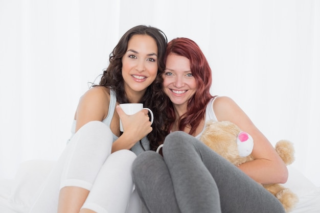 Glückliche junge Freundinnen mit Kaffeetassen im Bett