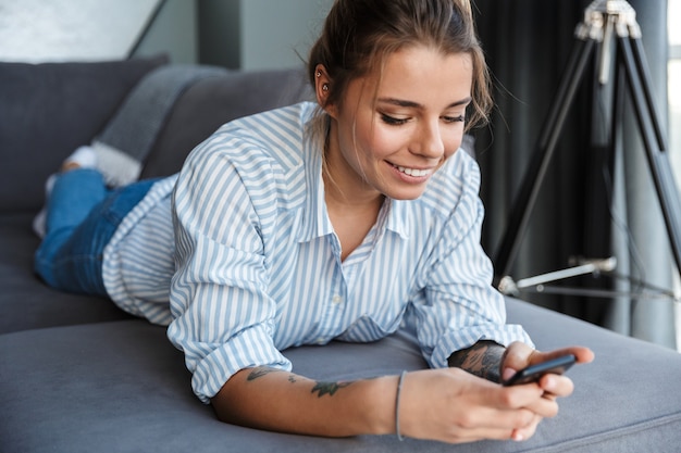 Glückliche junge Geschäftsfrau mit Handy beim Entspannen auf einer Couch zu Hause