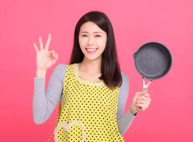 Glückliche junge Hausfrau trägt Küchenschürze und zeigt eine Geste „OK“.