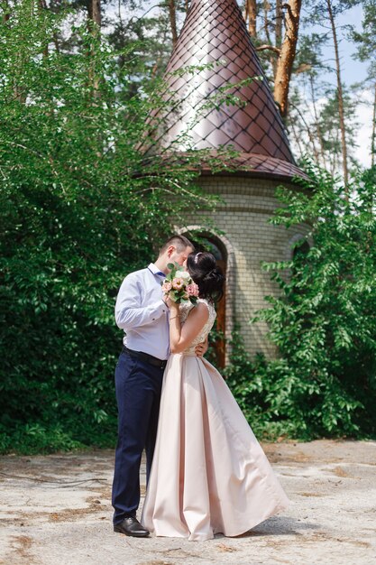 Glückliche junge Jungvermählten, die an ihrem Hochzeitstag umarmen und küssen. Braut und Bräutigam gehen bei der Hochzeit in der Natur. romantischer Moment auf dem Datum. Paar in der Liebe im Freien