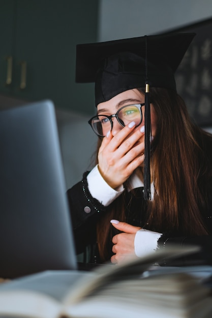 Glückliche junge kaukasische Frau, die Hochschulabschluss während eines Videoanrufs mit Freunden feiert