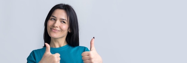 Glückliche junge kaukasische Frau in einem blauen T-Shirt, die Daumen hoch macht und lächelt Gute Arbeit