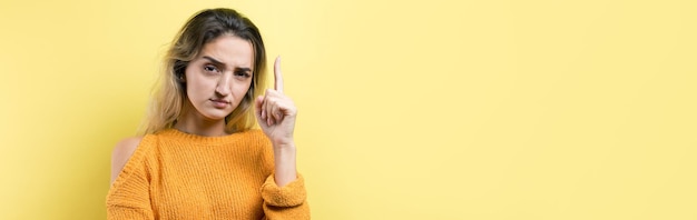 Glückliche junge kaukasische Frau in einem gelben Pullover, der die Finger weg zeigt.