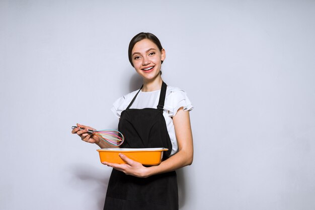 Glückliche junge Köchin in schwarzer Schürze, die eine köstliche Mahlzeit zum Abendessen zubereitet