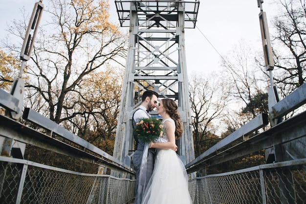 Glückliche junge lächelnde Braut und Bräutigam stehen auf der Hängebrücke. Hochzeitsfotos an einem interessanten Ort