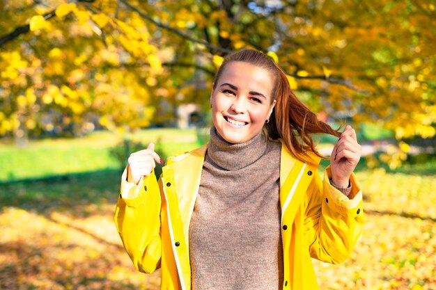 Glückliche junge lächelnde Frau, die im goldenen Herbst im Park geht