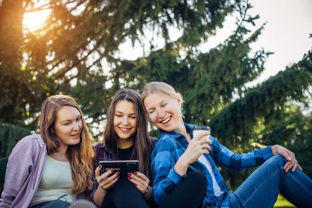 Glückliche junge Mädchen haben Spaß beim Lachen, das auf grünem Gras im Park sitzt