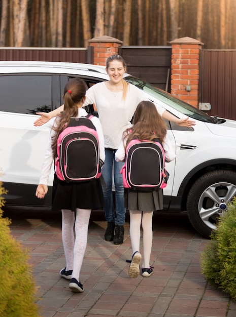 Glückliche junge Mutter, die ihre beiden Töchter nach der Schule im Auto trifft