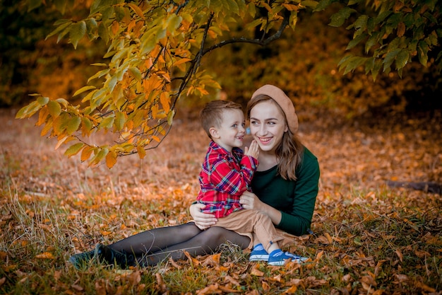 Glückliche junge Mutter, die Spaß mit ihrem kleinen Jungen am Herbsttag hat