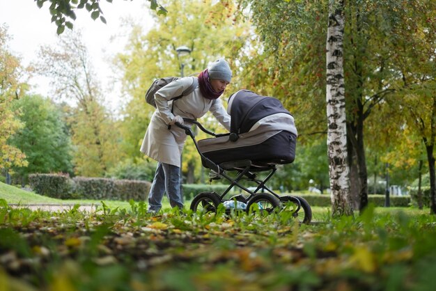 Glückliche junge Mutter mit Kinderwagen während des Spaziergangs in der Natur im Park