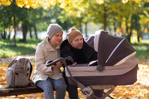 Glückliche junge Mutter mit Kinderwagen während des Spaziergangs in der Natur im Park