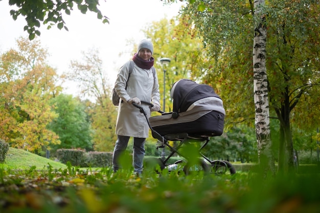 Glückliche junge Mutter mit Kinderwagen während des Spaziergangs