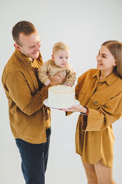 Glückliche junge Mutter und Vater halten ihren neugeborenen Sohn in ihren Armen und geben ihm einen Kuchen Eltern feiern ihren Geburtstag mit ihrem kleinen Sohn Das Konzept der Familienferien
