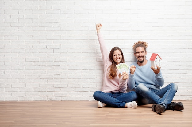 Glückliche junge Paare, die auf dem Boden ihres neuen Hauses sitzen. Konz