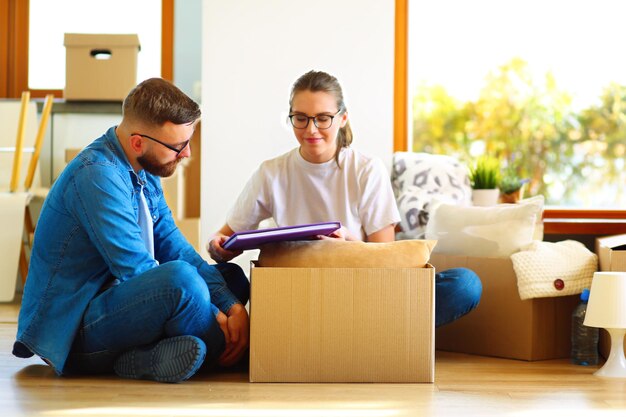 Glückliche junge Paare, die Kästen auspacken oder verpacken und in ein neues Haus umziehen