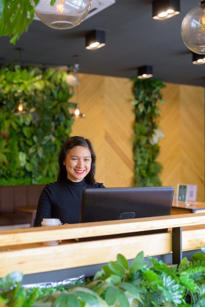 Glückliche junge schöne asiatische Geschäftsfrau, die Laptop am Kaffeehaus verwendet