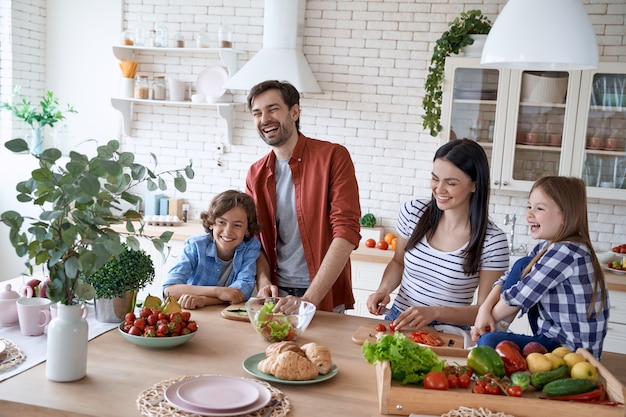 Glückliche junge schöne Familie, die zusammen einen Salat in der modernen Küche zu Hause zubereitet Mutter