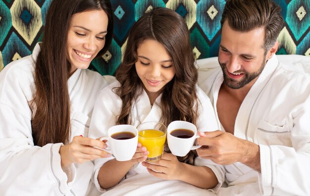 Glückliche junge schöne Familie in Bademänteln frühstücken morgens in einem Luxushotelzimmer