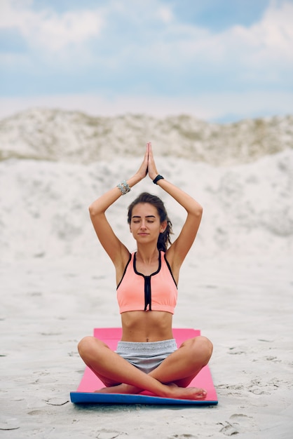 Glückliche junge schöne Frau, die Yoga am Strand bei Sonnenuntergang praktiziert