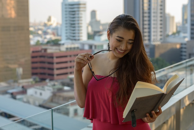 Glückliche junge schöne indische Frau, die Buch gegen Ansicht der Stadt liest