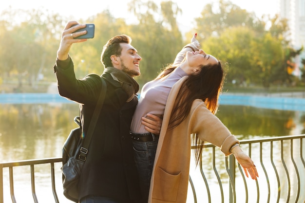 glückliche junge schöne liebevolle Paare, die draußen in der Parknatur spazieren gehen, nehmen selfie mit dem Handy.