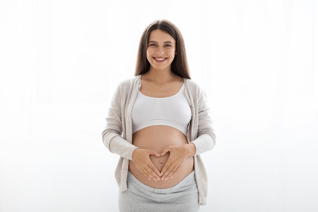 Glückliche junge schwangere Frau, die Hände auf dickem Bauch hält