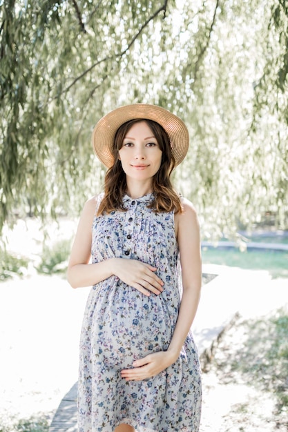 Glückliche junge schwangere Frau im Park an einem Frühlings- oder Sommertag