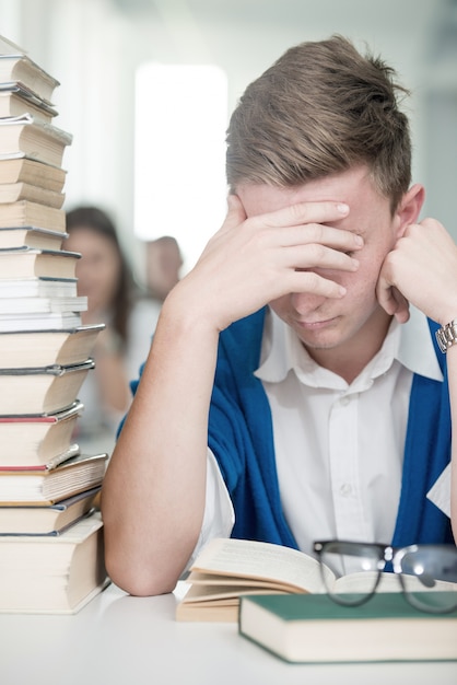 Glückliche junge Studenten, die in der Collegebibliothek mit Stapel Büchern studieren