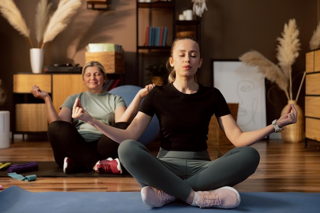 Glückliche junge Tochter mit Frau mittleren Alters, die die Augen schließt, die auf einer Yogamatte sitzen und Yoga-Übungen meditieren