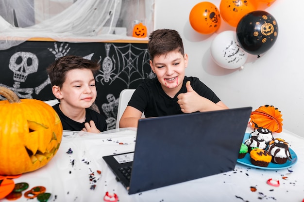 Glückliche Jungen, Brüder, die mit Großeltern oder Freunden per Videoanruf unter Verwendung eines Laptops am Halloween-Tag sprechen, aufgeregte Jungen in Kostümen, die Computer betrachten Daumen zeigen