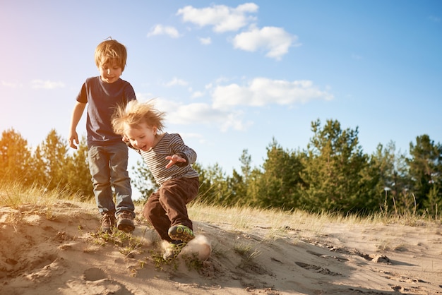 Glückliche Jungen, die am sonnigen Tag auf Sand springen