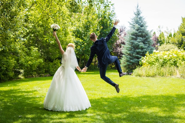 Glückliche Jungvermählten freuen sich und springen auf einen grünen Rasen. Frau weißes Hochzeitskleid, Bräutigam im Anzug.