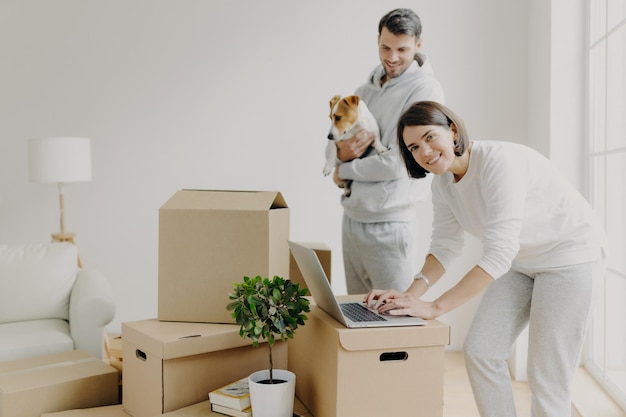 Glückliche Käufer von Eigenheimen posieren in der Nähe von ausgepackten Kisten und genießen den Umzug in ein neues Haus