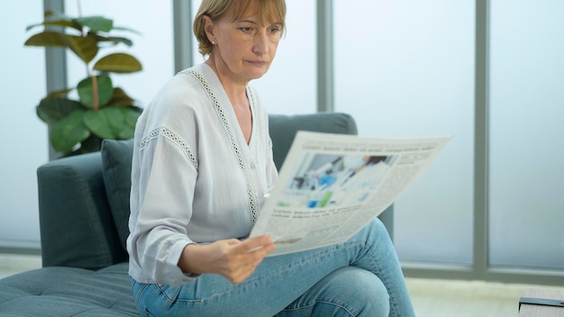 Glückliche kaukasische ältere Frau entspannt sich und liest Zeitung im Wohnzimmer