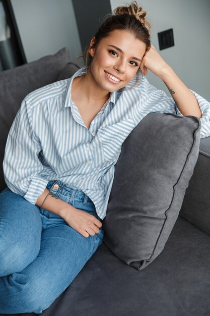 Foto glückliche kaukasische frau im gestreiften hemd, die lächelt, während sie auf dem sofa im wohnzimmer sitzt