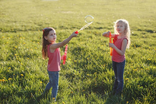 Glückliche kaukasische Mädchen, die an einem Sommertag Seifenblasen im Park blasen, Kinder, die sich im Freien amüsieren.