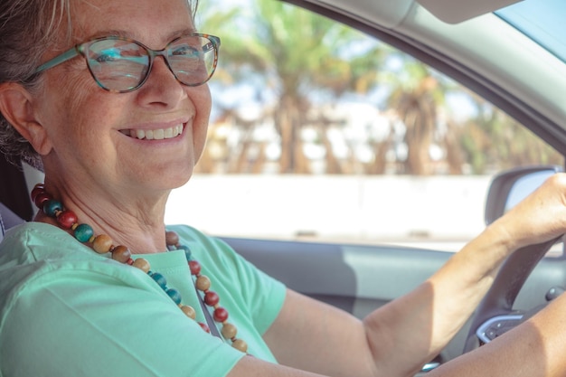 Glückliche kaukasische Seniorin, die das Auto fährt und lächelnd in die Kamera schaut